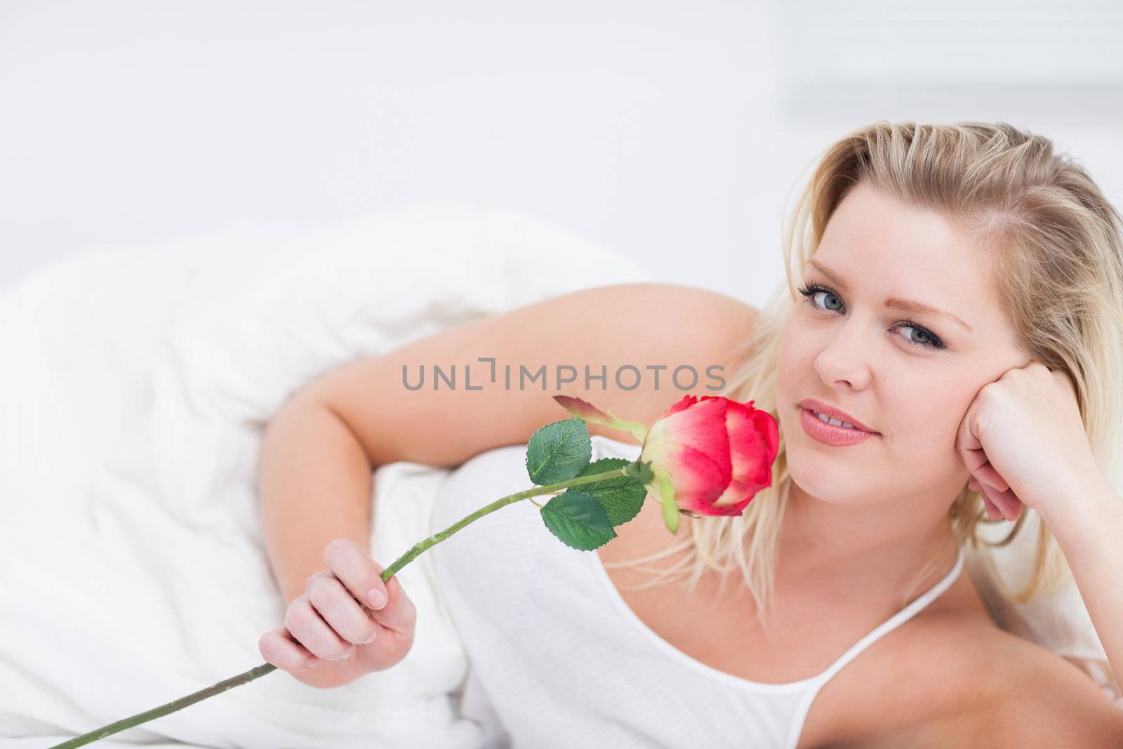 Young woman holding a pink rose while lying on her bed