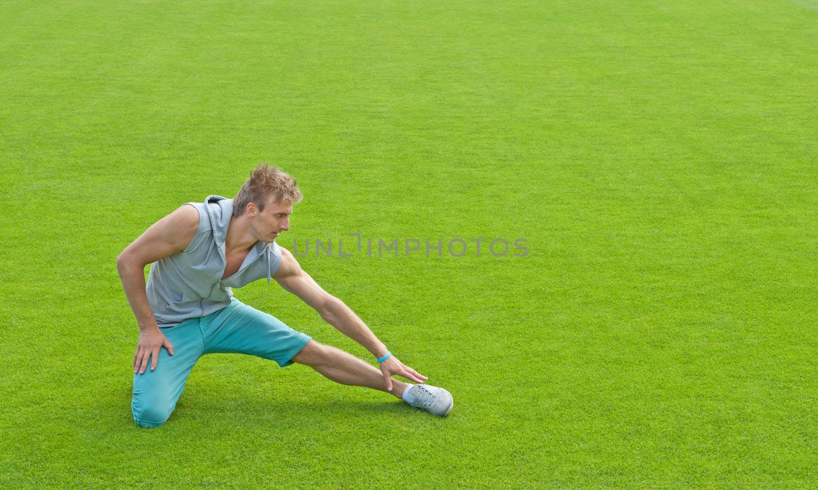 Fit young man exercising outdoors on green sports field.