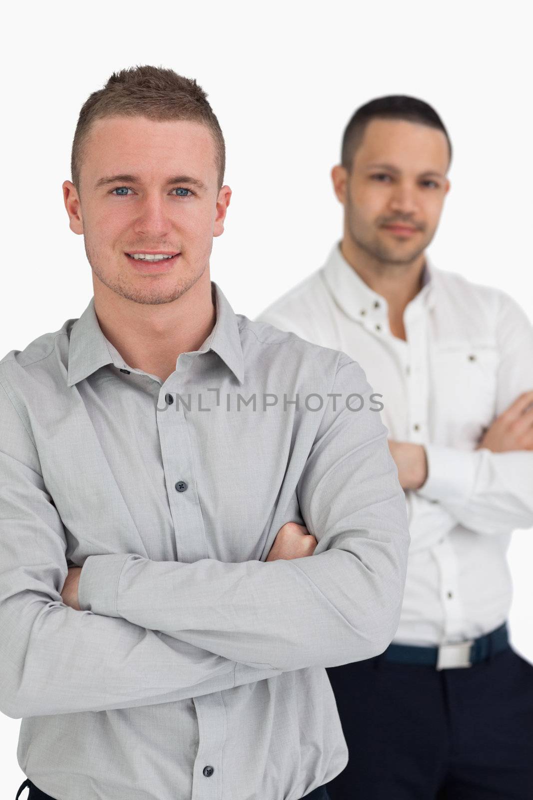 Two men smiling while crossing their arms against a white background