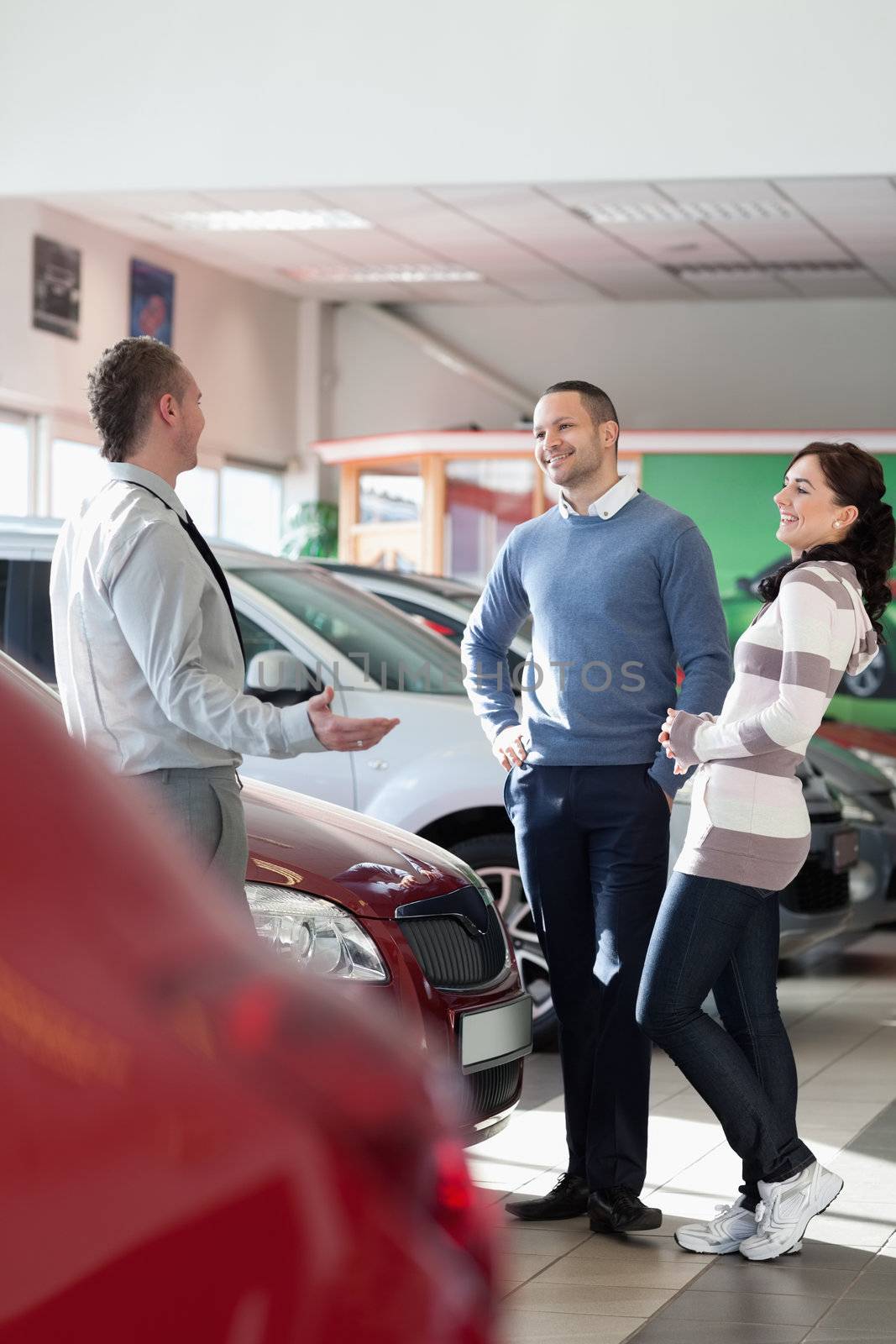 Smiling couple talking with a car dealer in a car shop