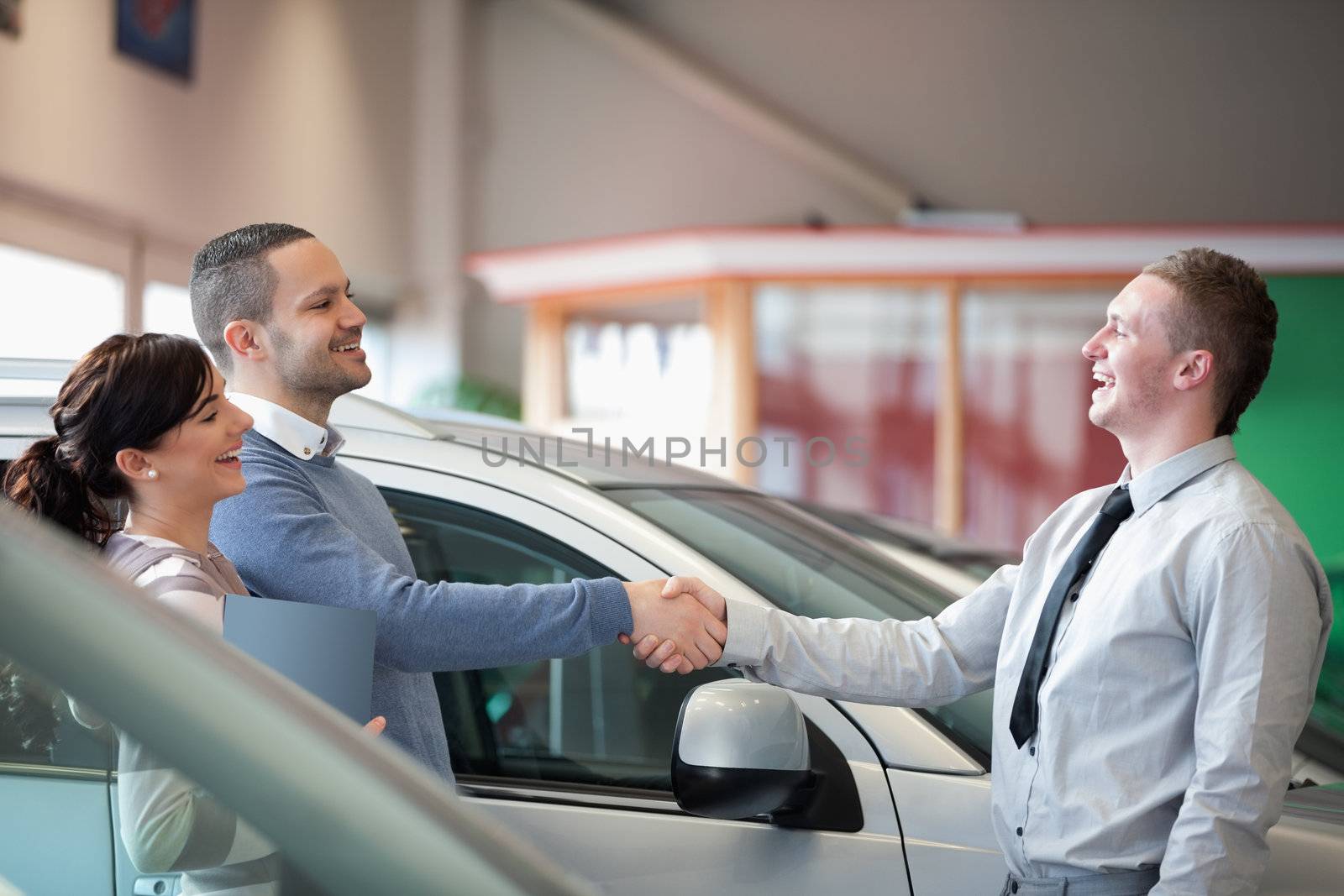 Salesman smiling while shaking the hand of a customer in a car shop