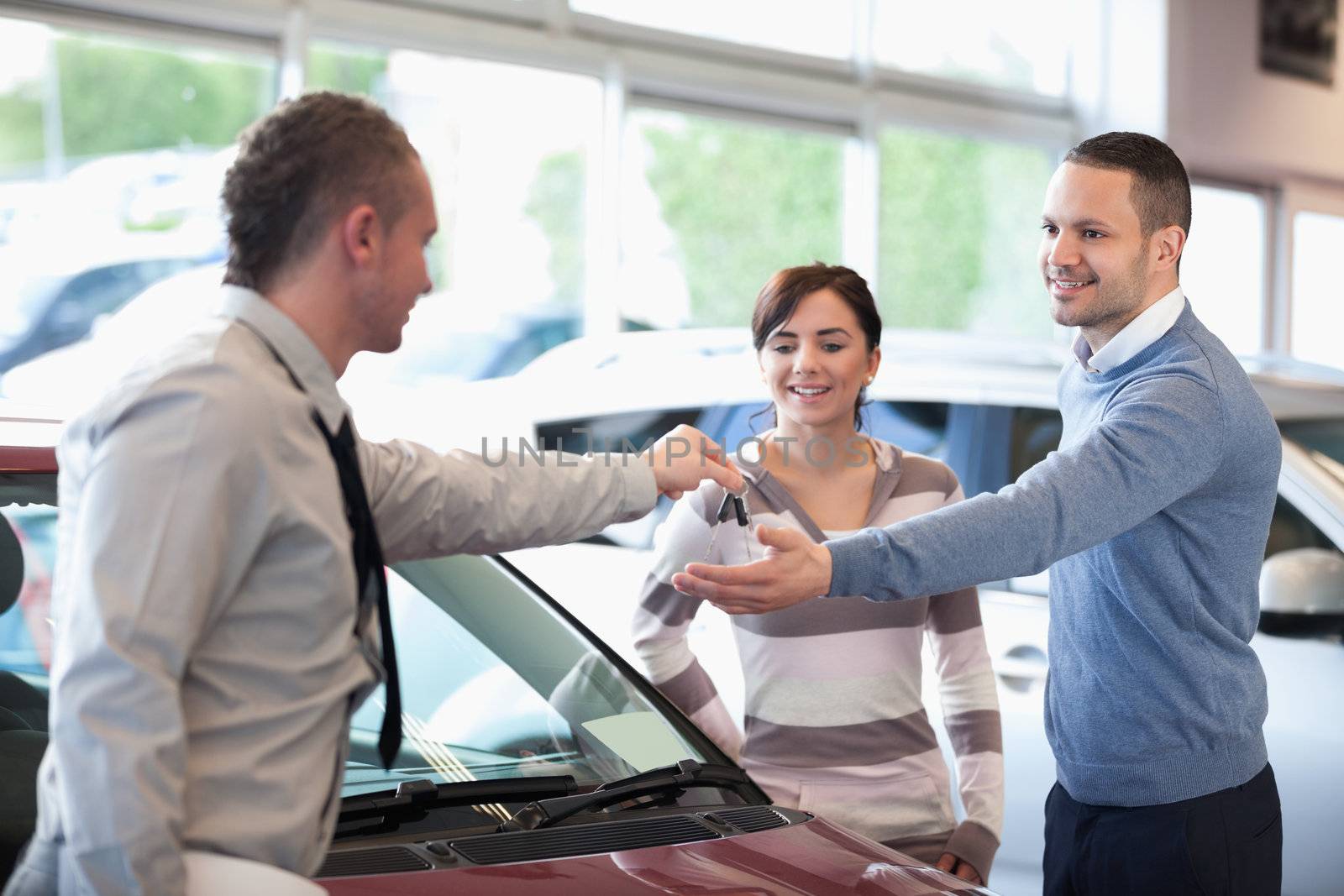 Smiling couple receiving keys from a car dealer in a car shop