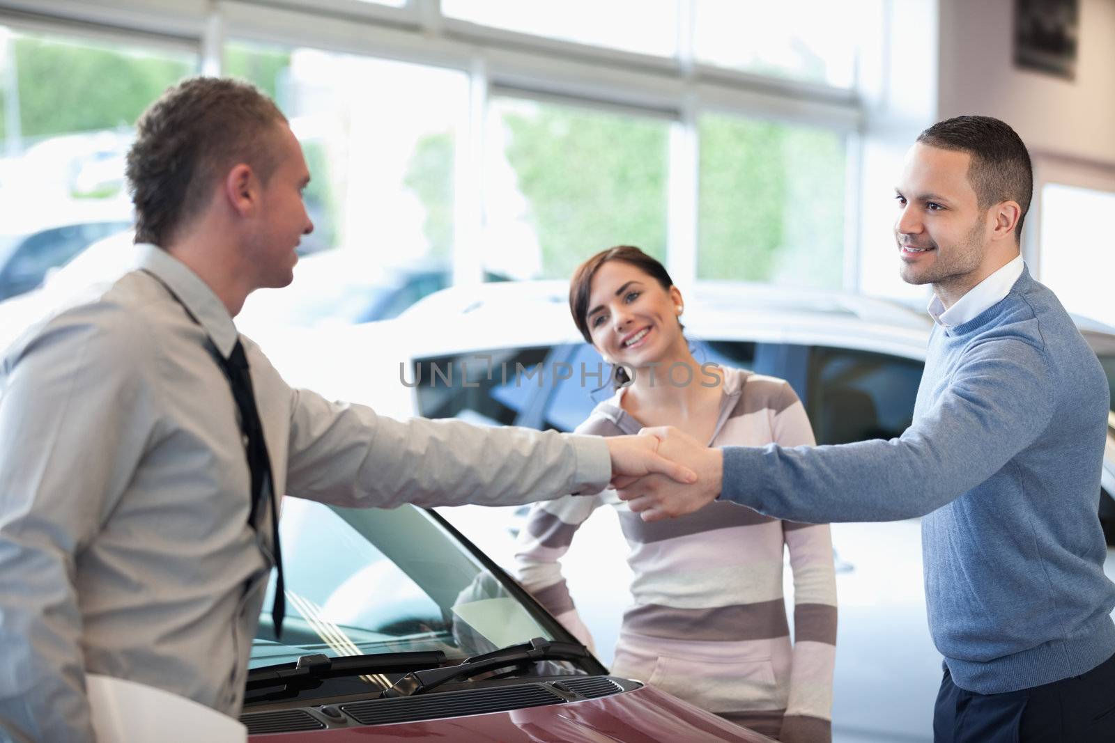 Car dealer shaking hand with a smiling man in a car shop