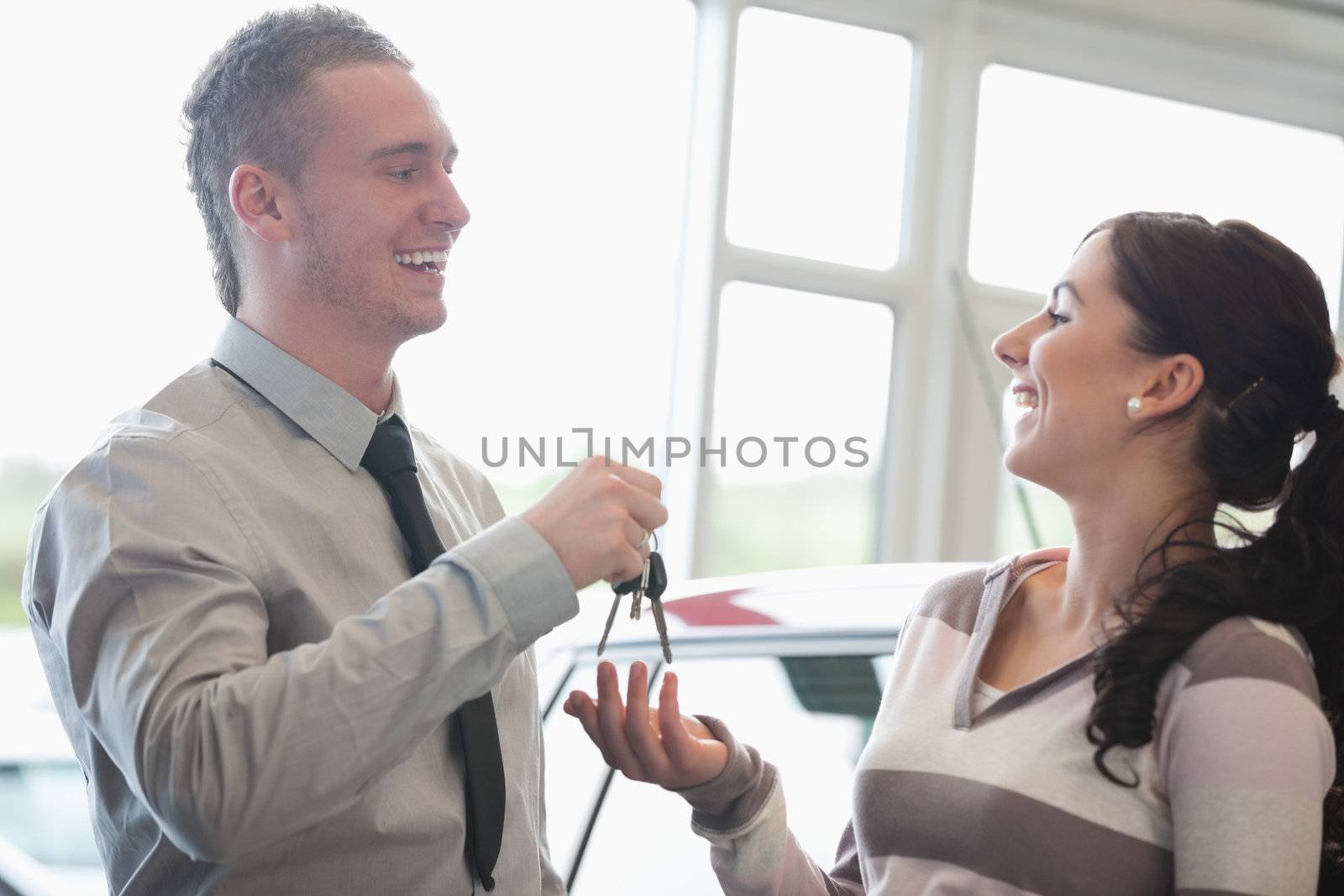 Laughing salesman giving keys to a woman in a car shop