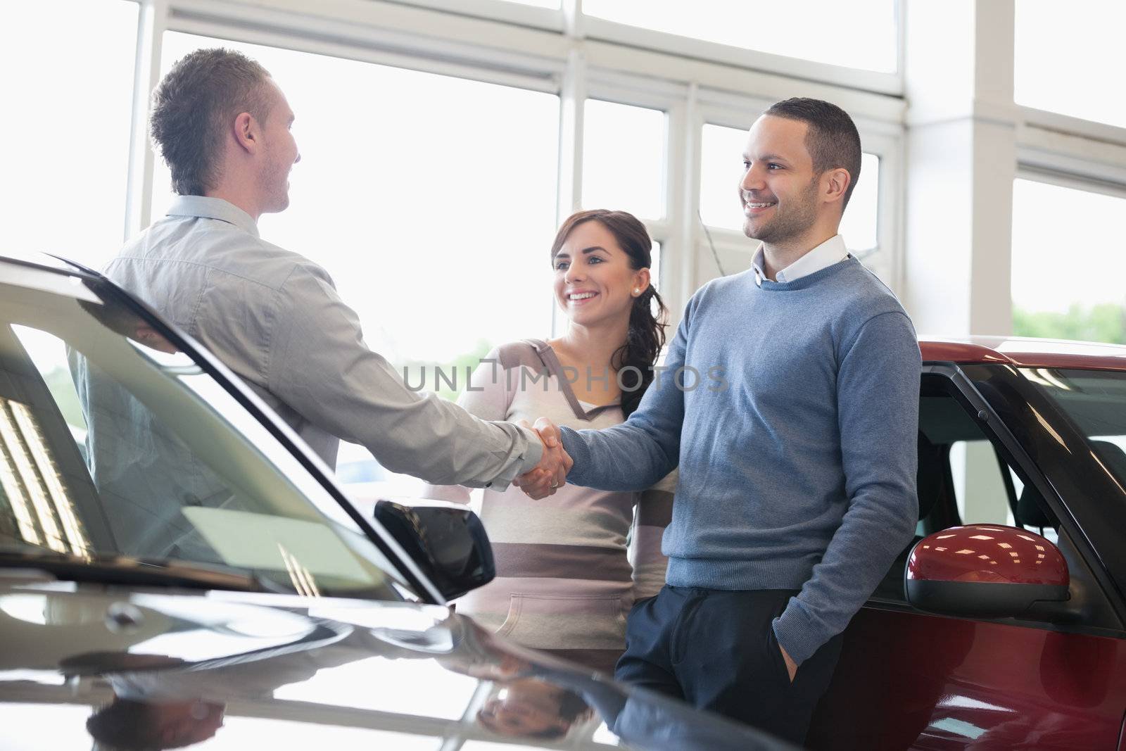 Man shaking a car dealer hand with his wife