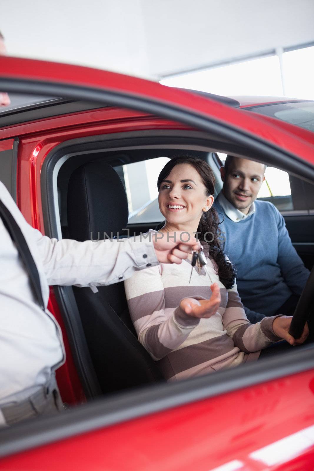 Smiling woman receiving keys from a salesman while sitting in a car