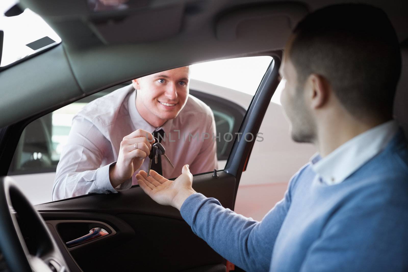 Smiling salesman giving keys to a customer in a car