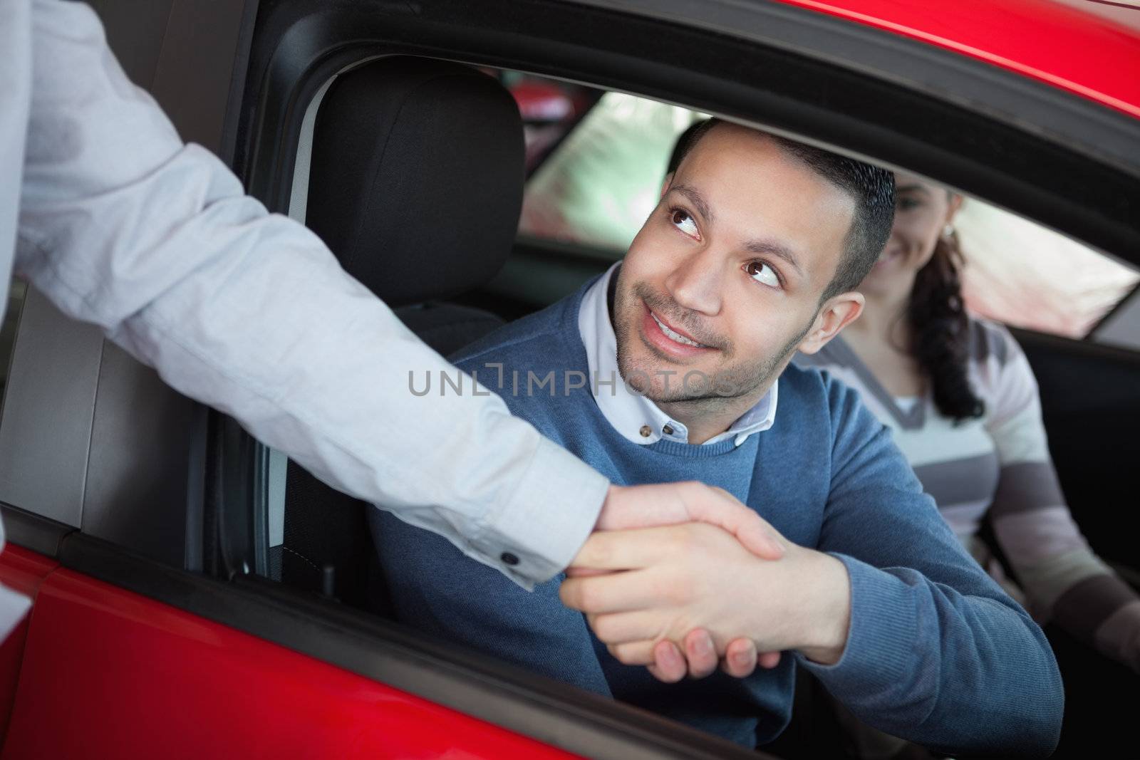 Man shaking the hand of a car dealer while sitting on a car