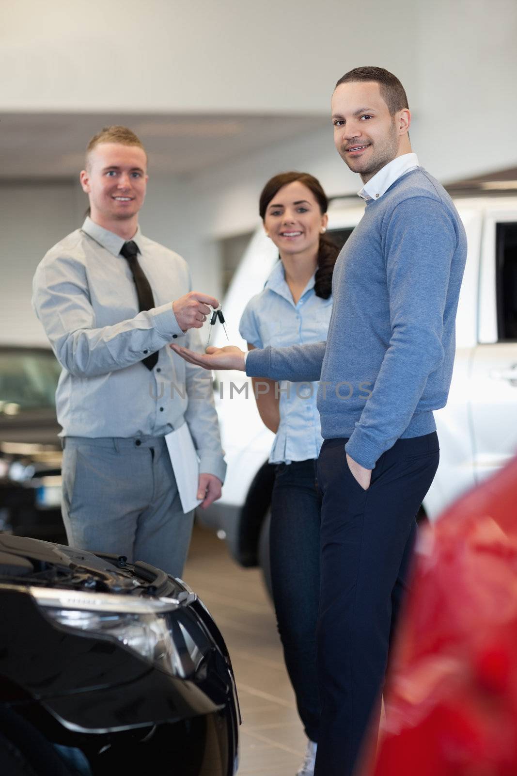 Smiling salesman handing keys to an happy couple in a car shop