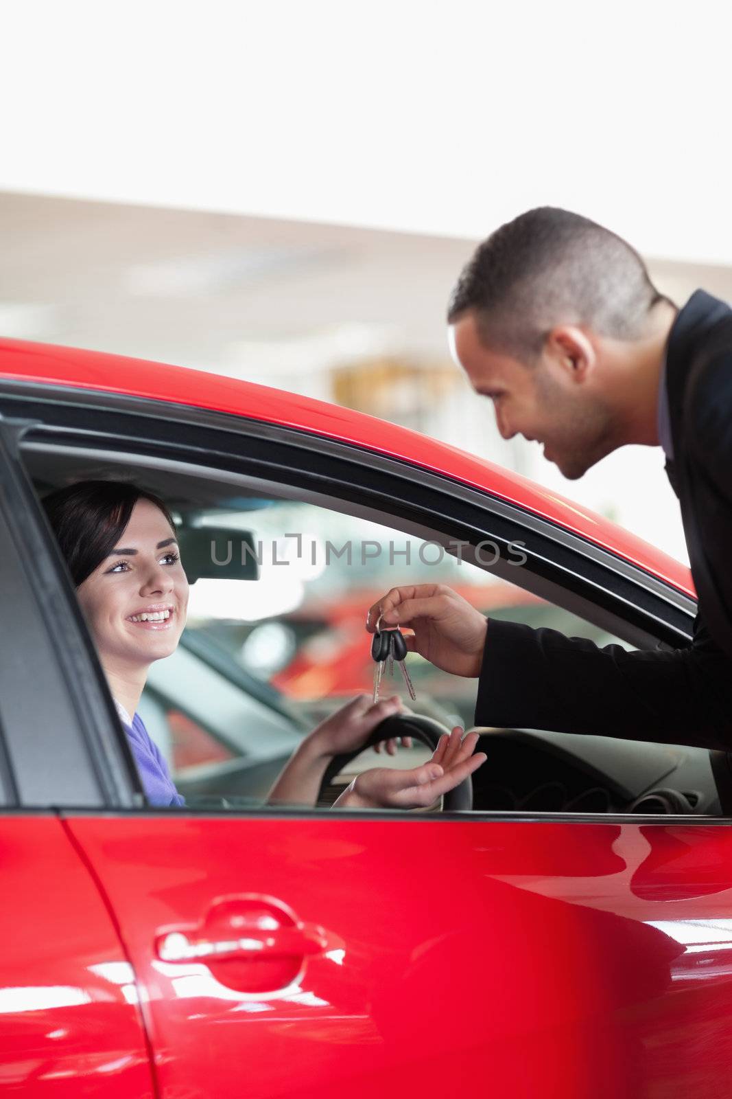 Smiling woman receiving car keys while sitting on a car