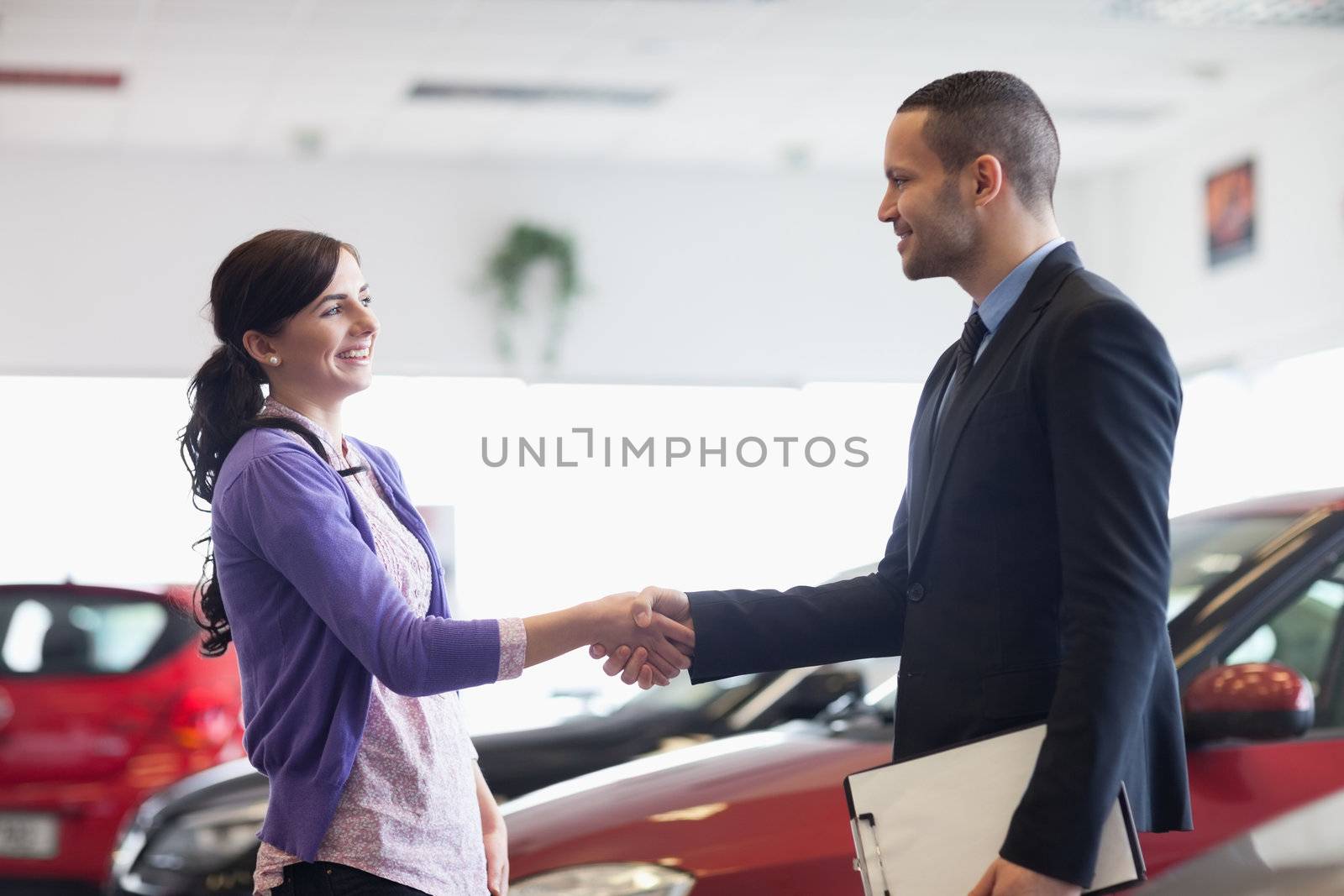 Salesman and a woman shaking hands in a car shop