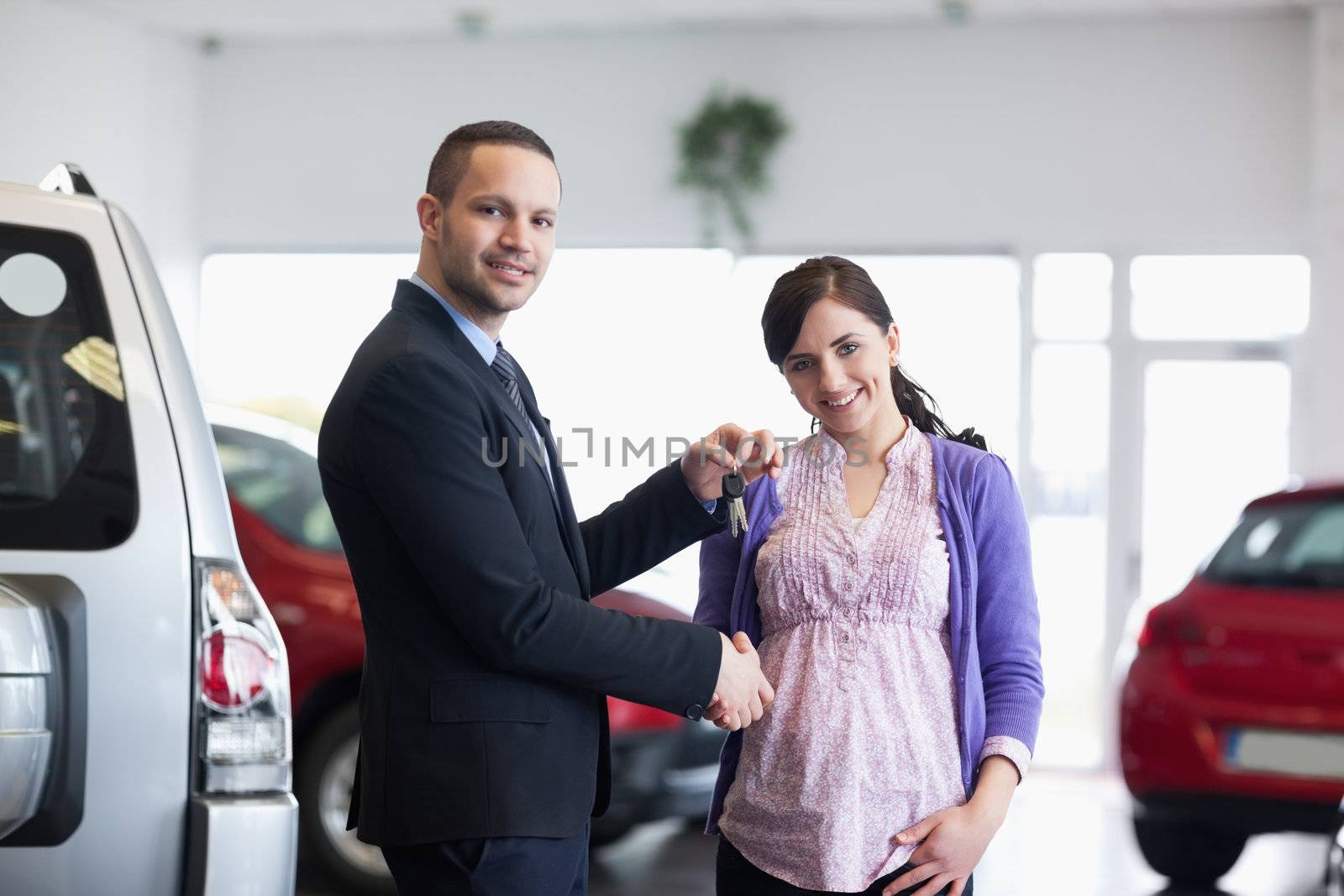 Salesman shaking hand and giving keys to a woman in a car shop