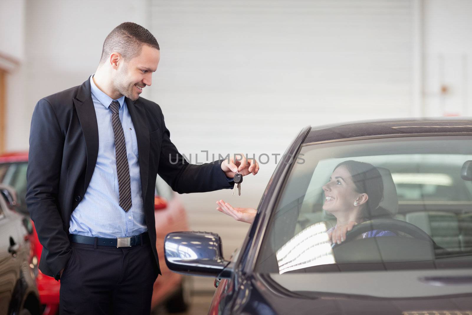 Salesman smiling while giving keys to a woman in a car dealership