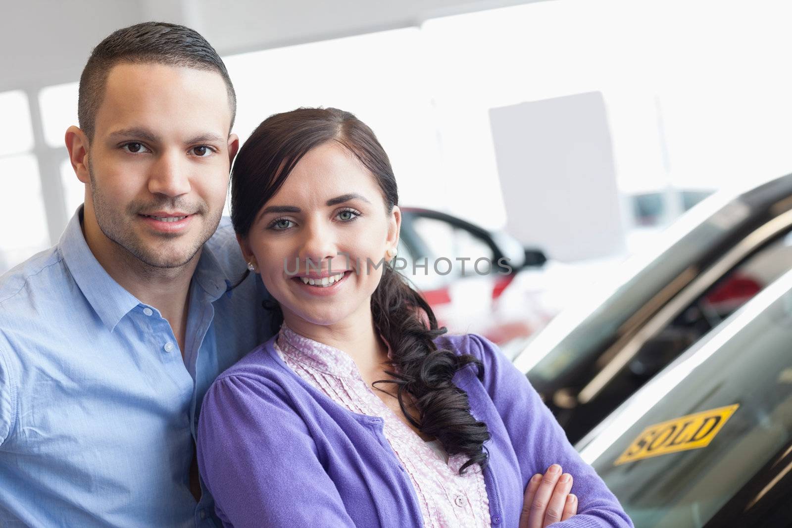 Couple hugging in front of a car in a car dealership