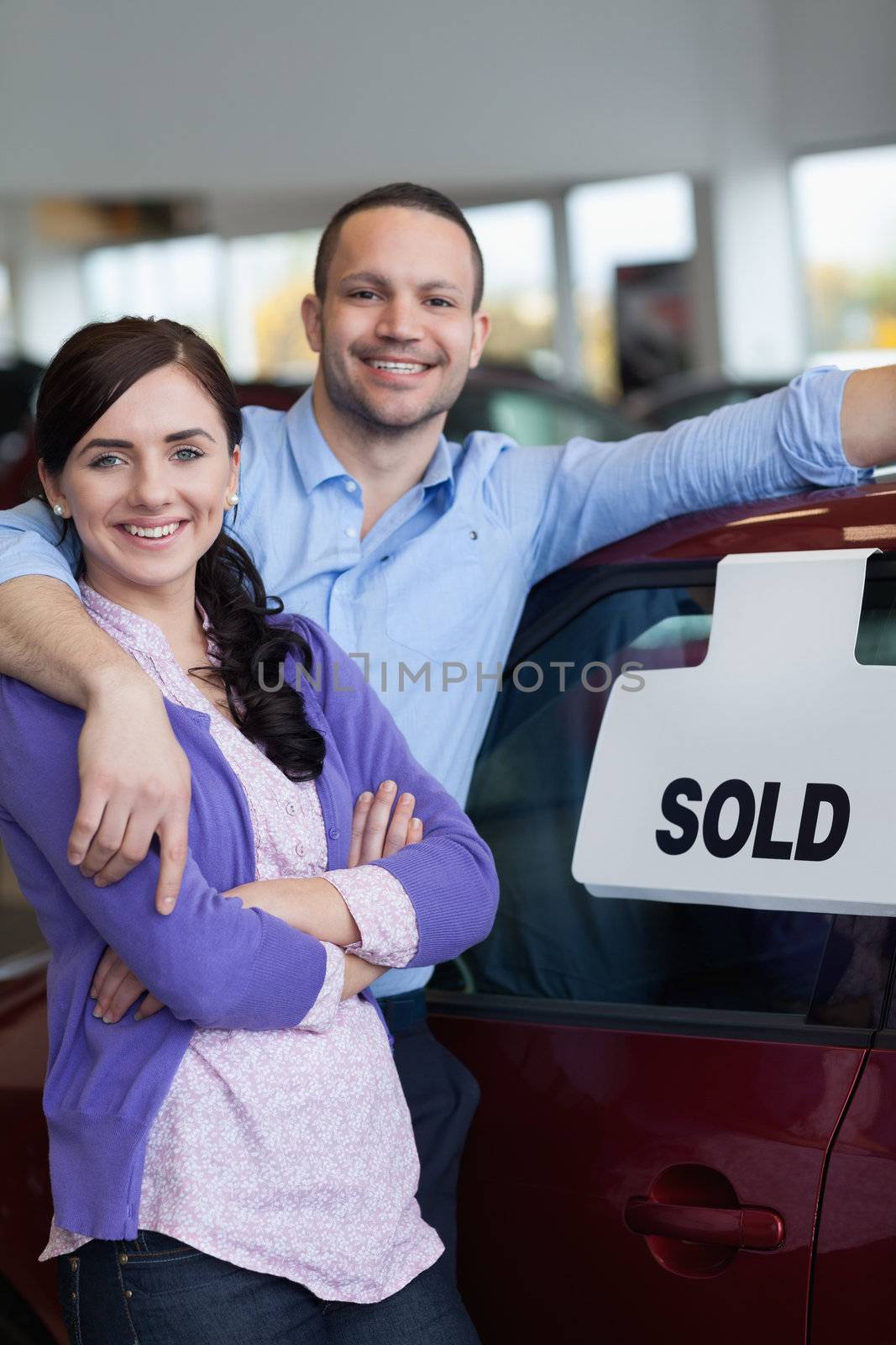 Smiling couple hugging in front of a car in a car dealership