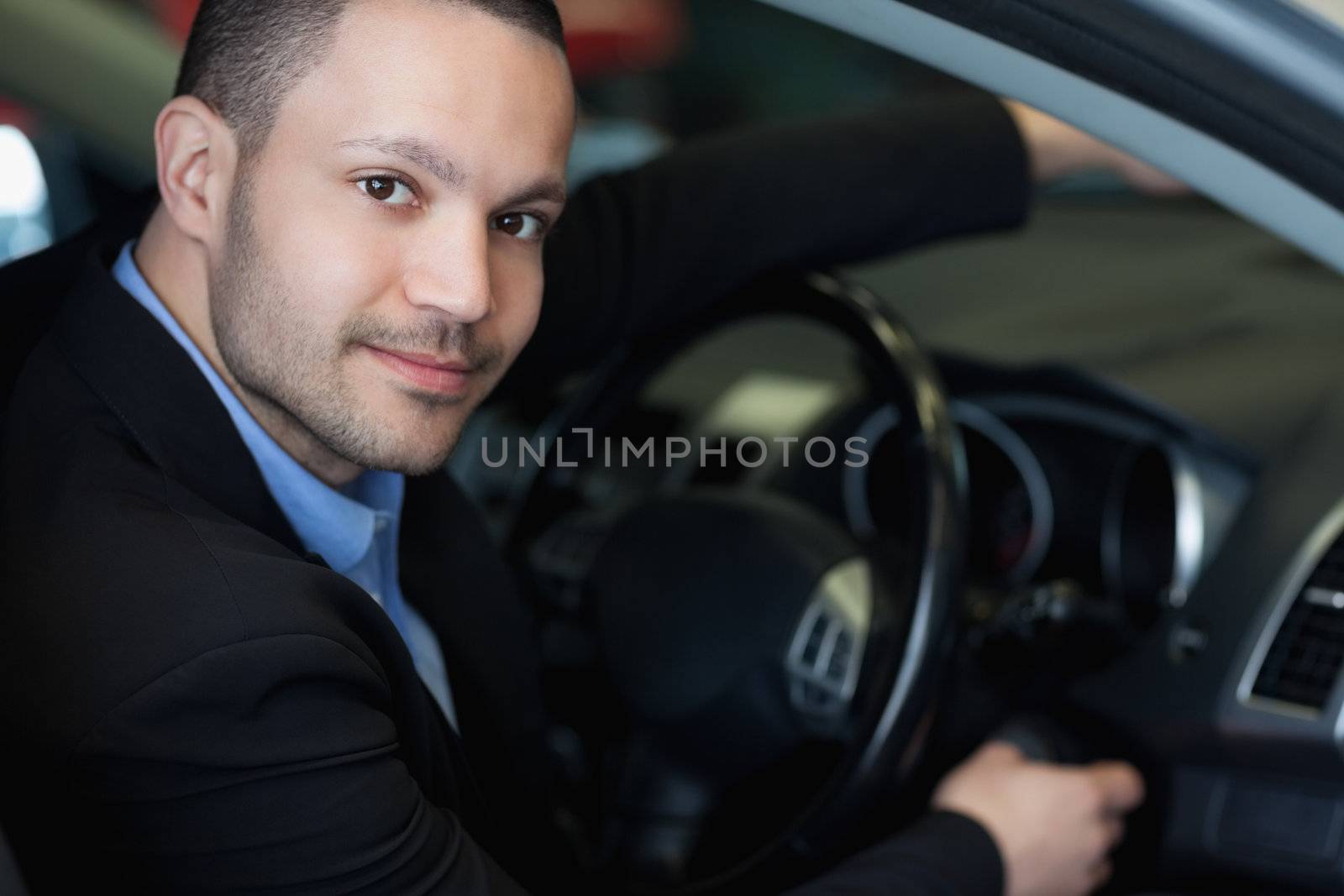 Man sitting on a car while turning on the engine in a car dealership