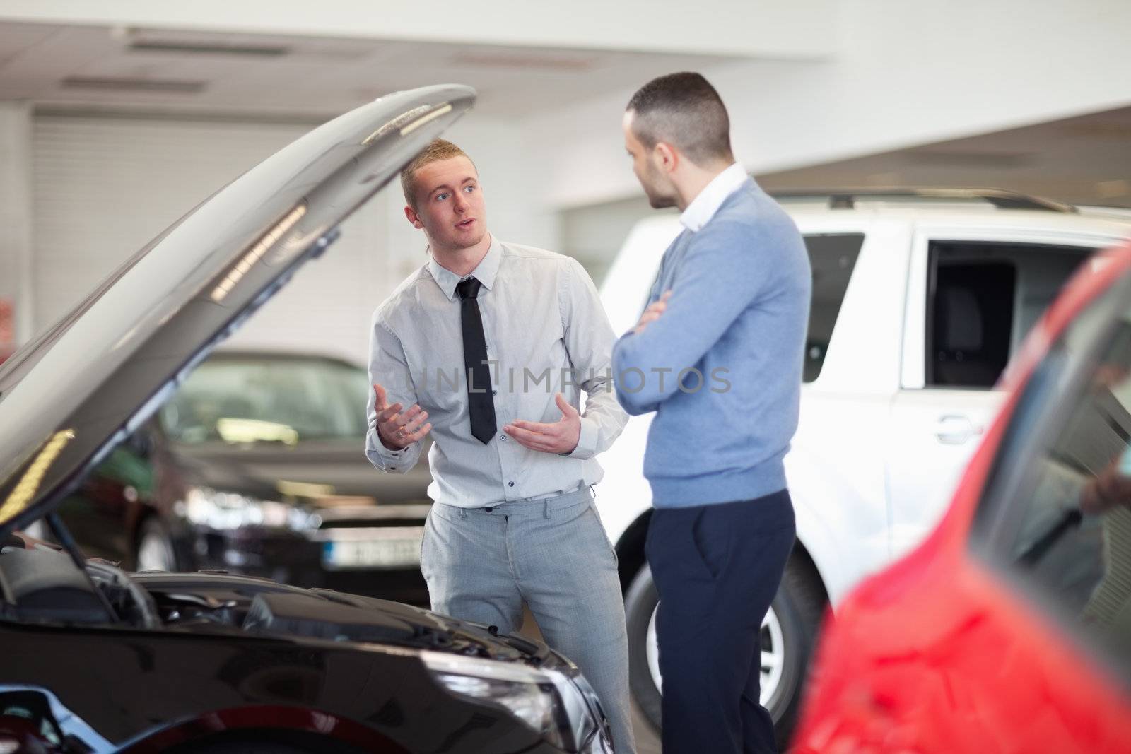 Two men chatting in front of an open engine in a car dealership