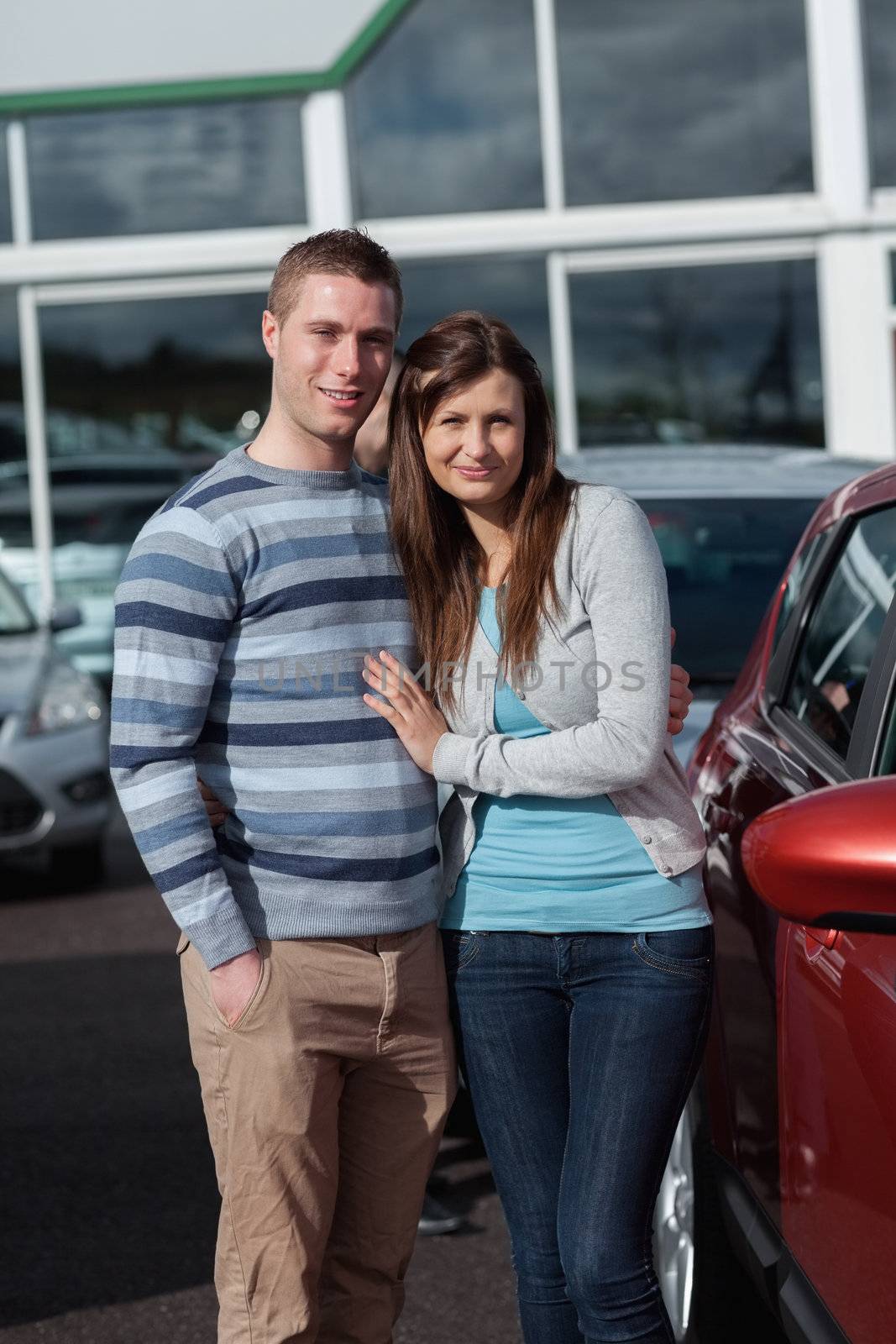 Couple holding tight while standing next to a car in a car park