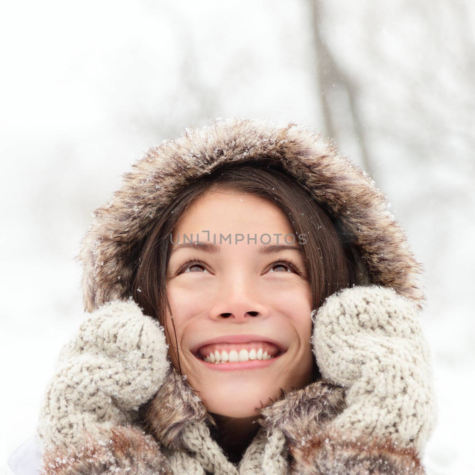 Winter woman looking up happy and smiling outdoors in snow on cold winter day. Asian girl model in her twenties.