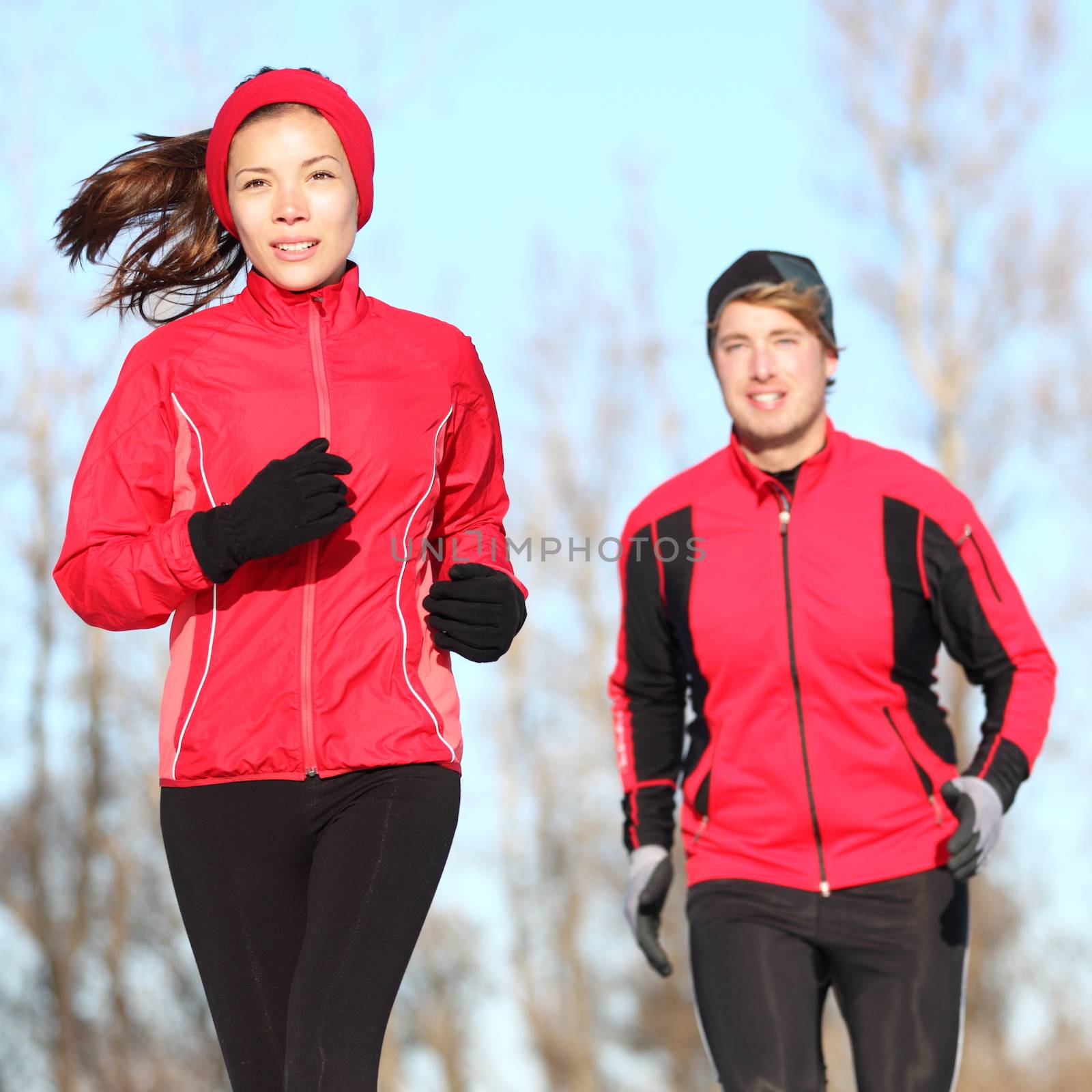 Healthy lifestyle winter running. Runner couple jogging in city park in warm winter sports clothing. Fit Asian woman fitness model and Caucasian man model.