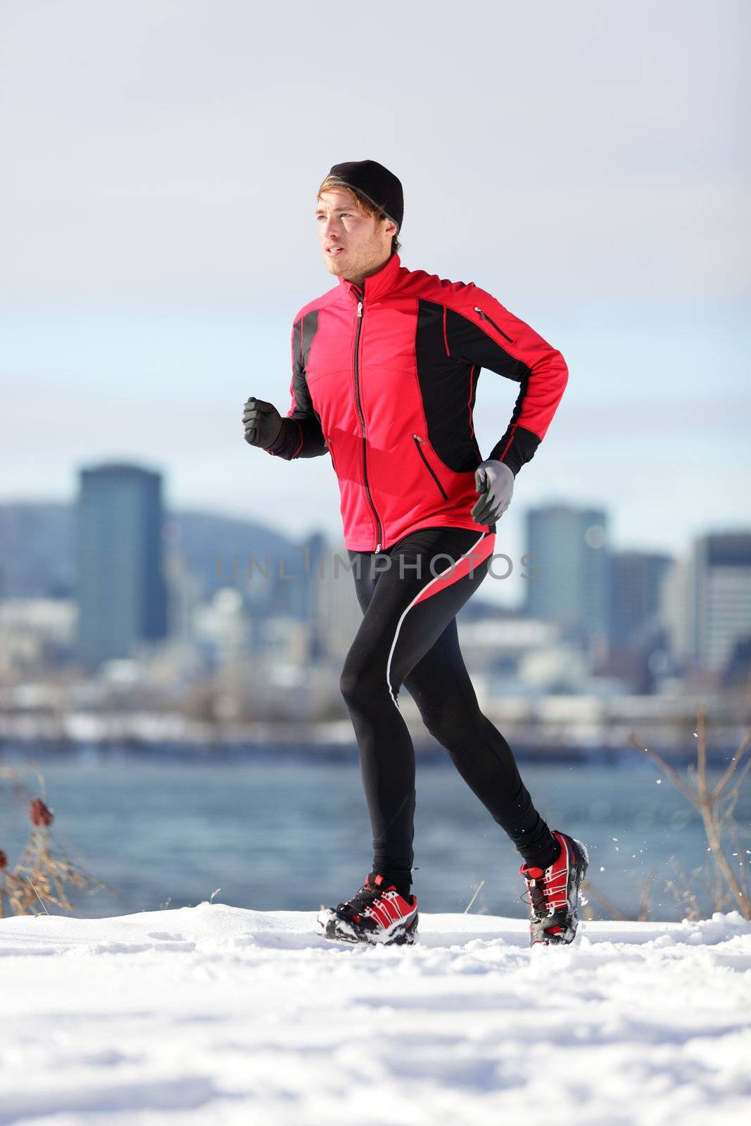 Fitness running man. Male runner training and jogging outdoors in winter snow with cityscape skyline in background. Wellness workout and healthy lifestyle concept with Caucasian male fitness model in Montreal, Quebec, Canada.