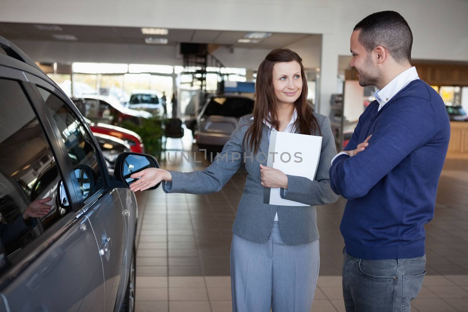Businesswoman presenting a car to a client in a dealership