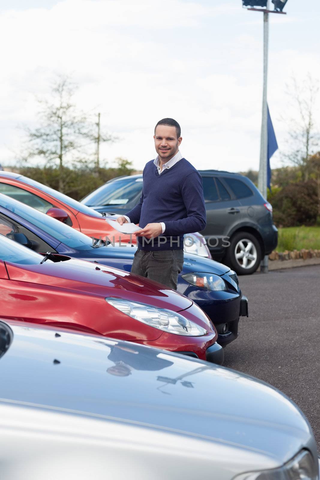 Man holding a folder in his hands while standing in a dealership parking