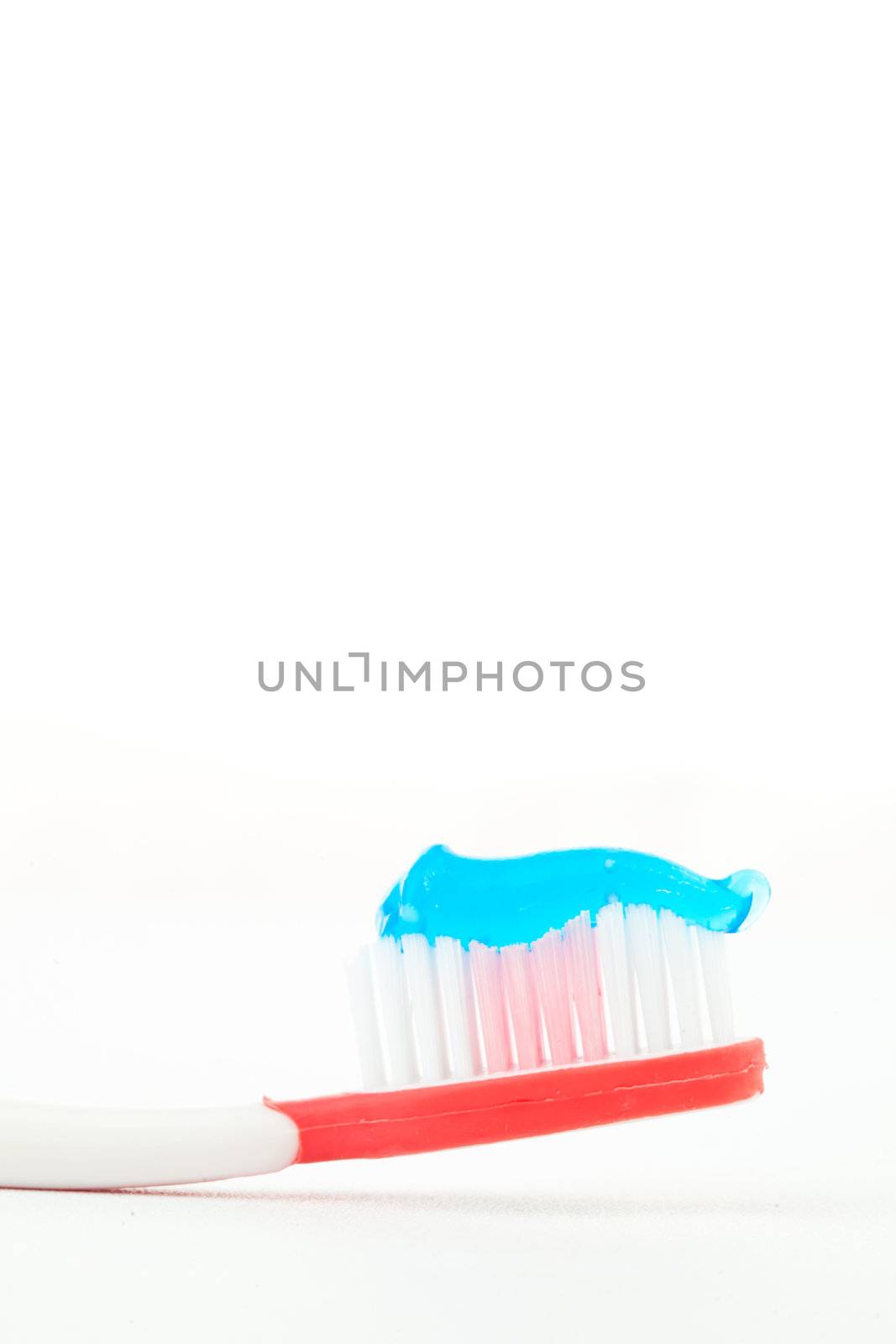 Blue toothpaste on a red toothbrush against white background