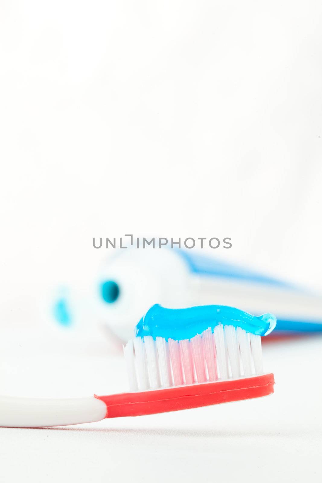 Red toothbrush next to a tube of toothpaste against white background