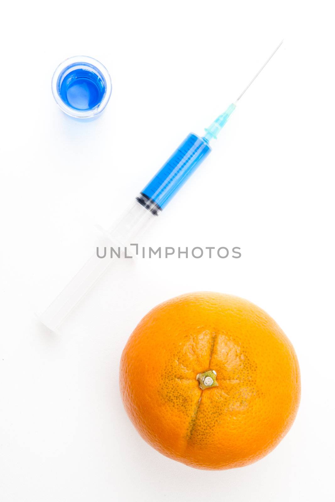  Syringe between a beaker and an orange against a white background