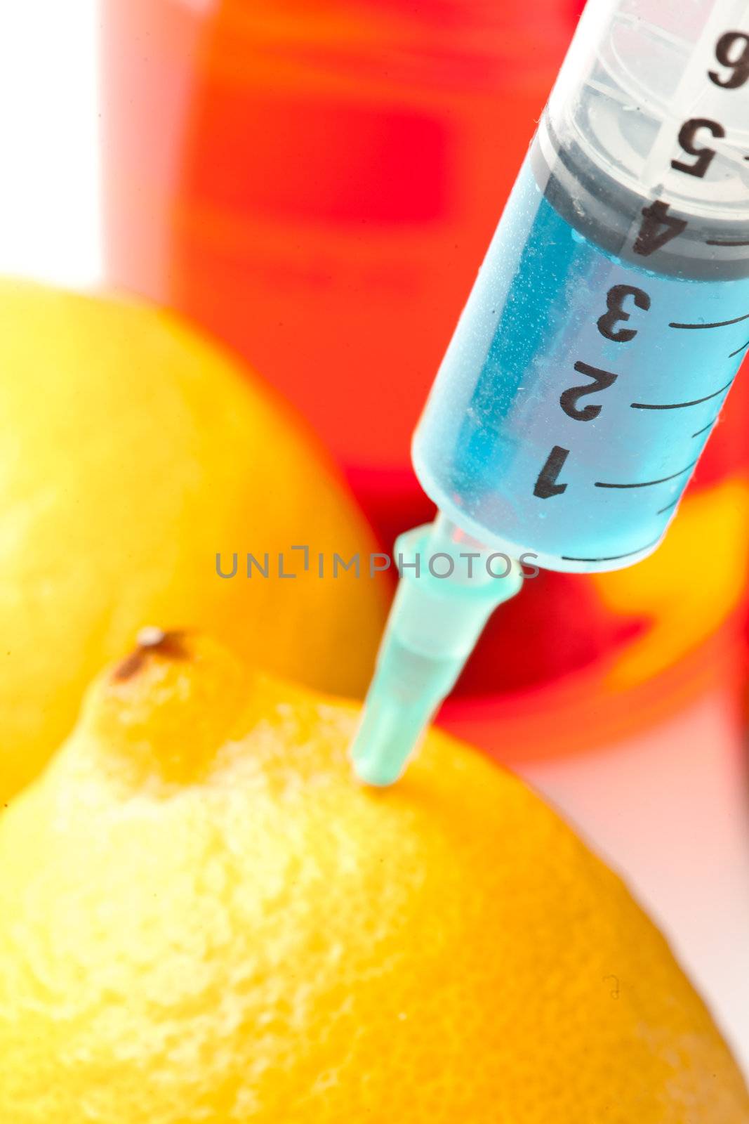 Close up of syringe into a lemon against a white background