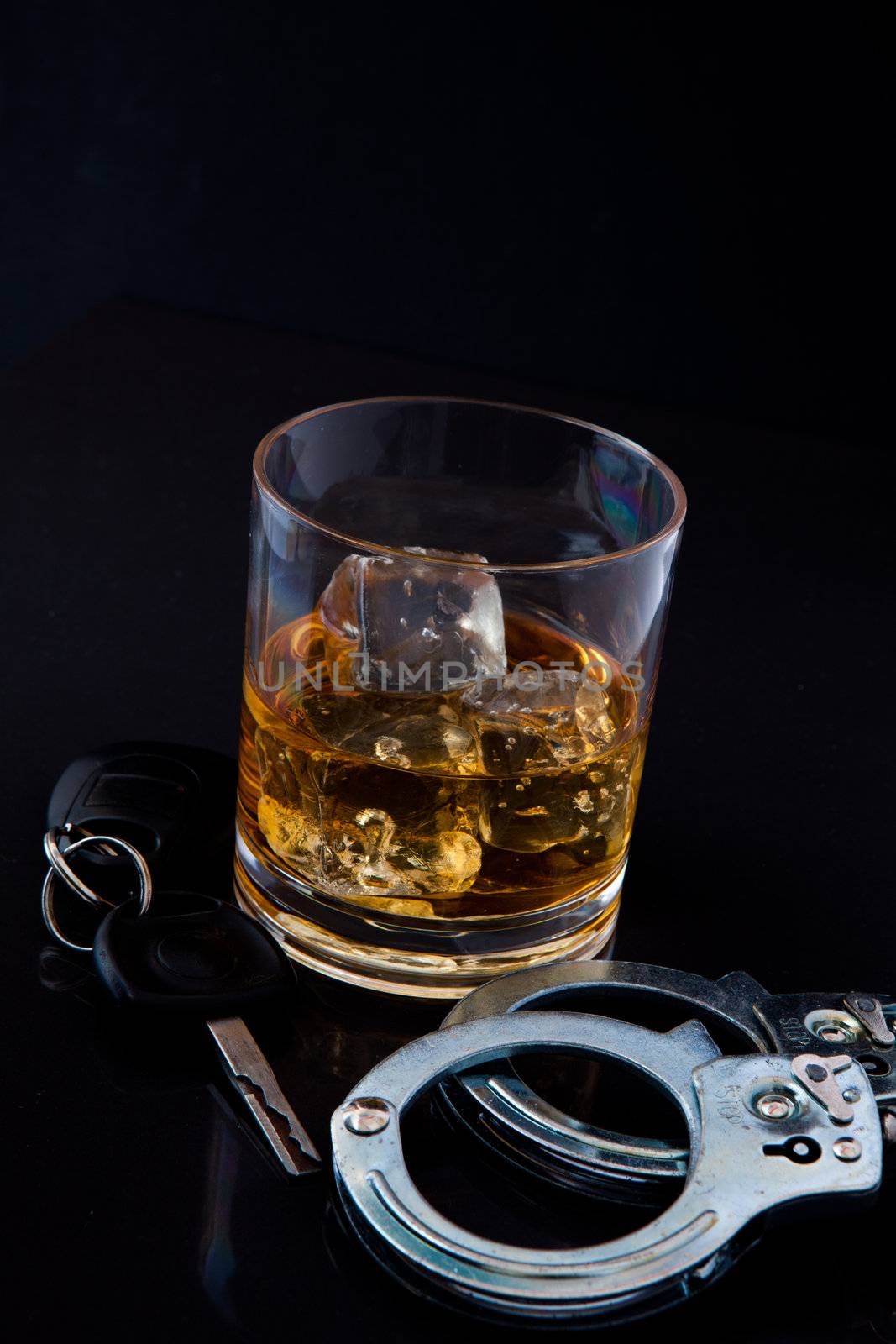 Whiskey on the rocks with car key and handcuff against a black background