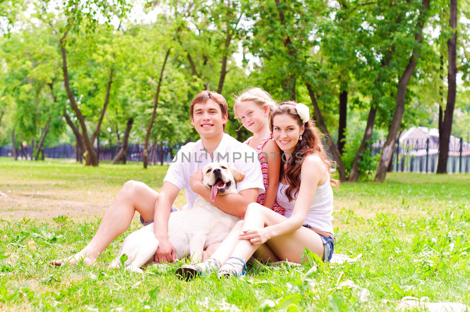 Happy young family with Labrador is resting in the park