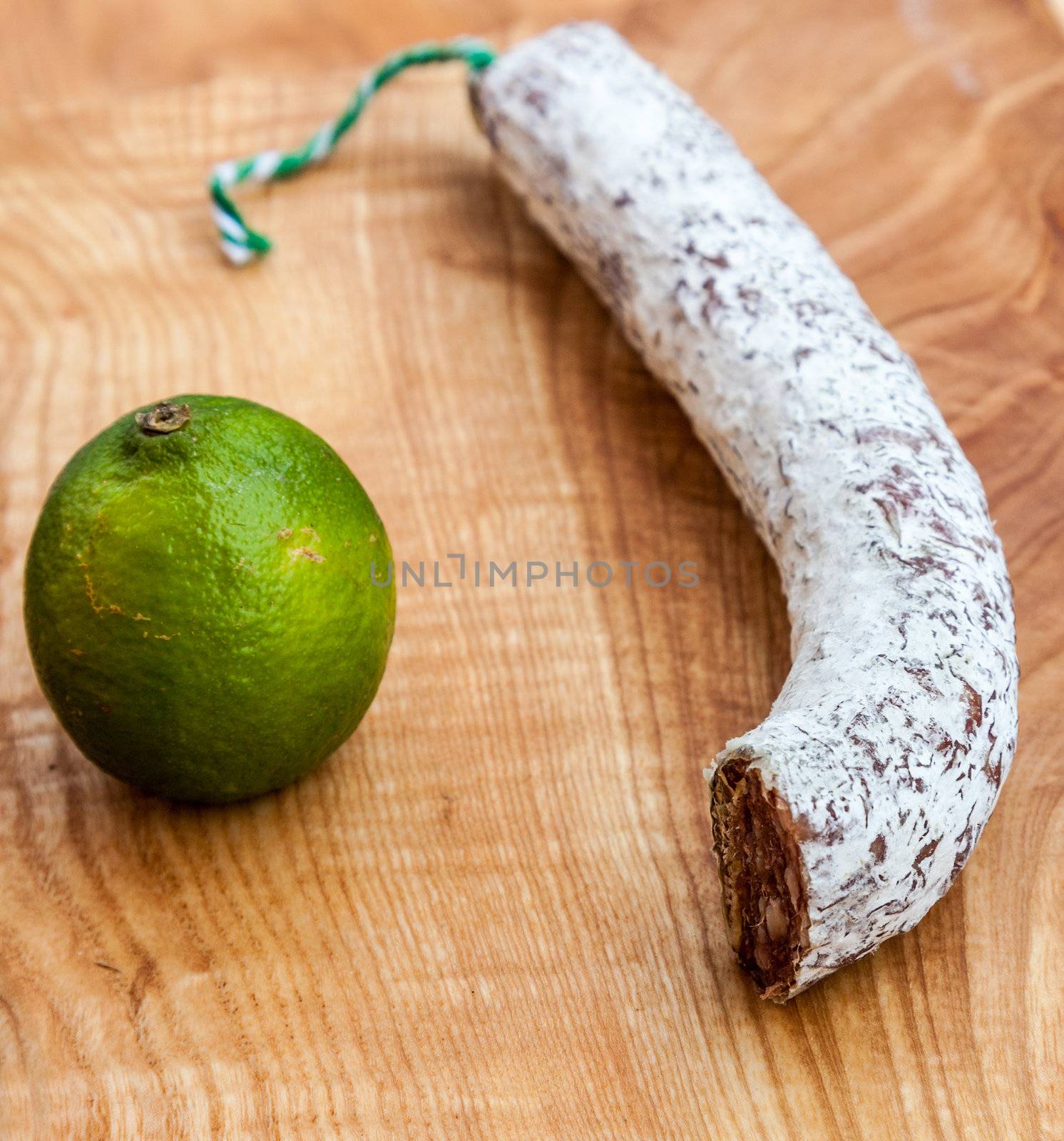 A piece of dried French sausage and a lime on a wooden board.