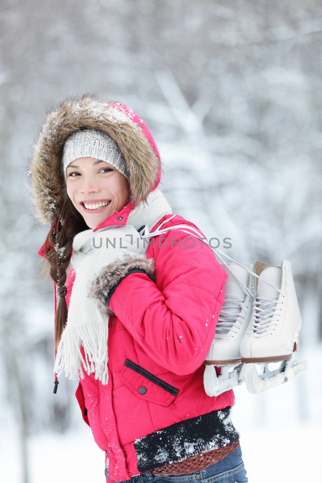 Beautiful young Asian woman smiling happily as she walks through wintery countryside with her ice skates over her shoulder