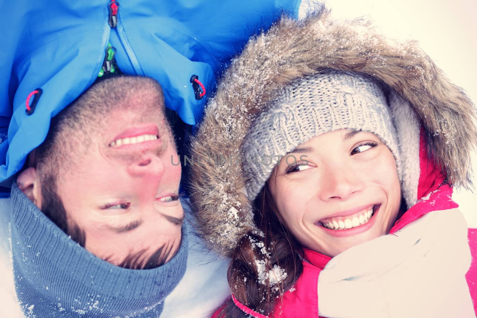 Happy winter couple. Cropped view of the faces of a joyful young interracial Asian / Caucasian couple lying on their backs in snow with their heads close together.