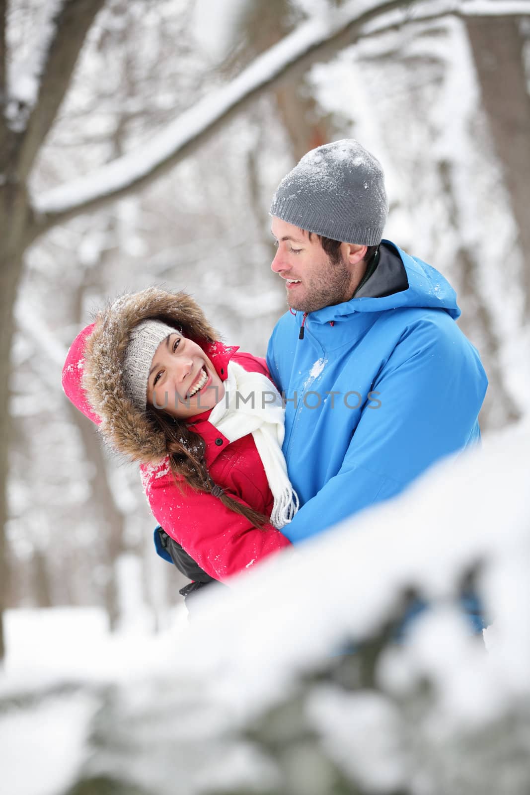 Romantic young couple holding each other in a close embrace and laughing merrily hugging in the snow