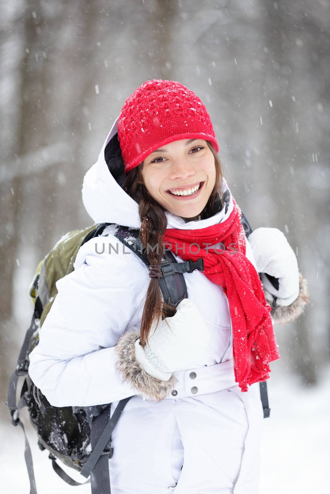Cheerful Asian woman with a lovely broad smile standing in warm winter clothes with a satchel on her back in falling snow