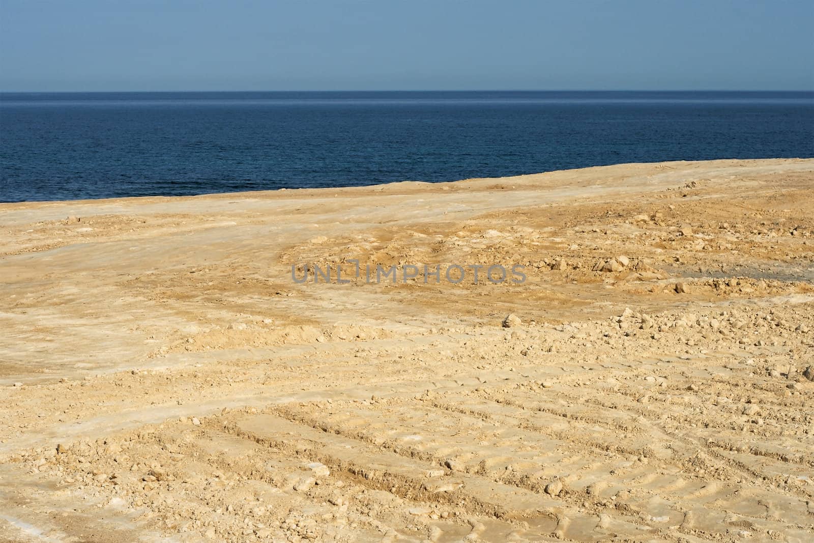 Scenic background of a beautiful empty sandy beach with tracks lit by the sun overlooking a blue tropical ocean