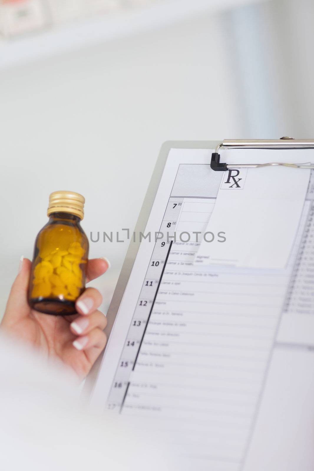 Hand holding bottle of drugs next to a clipboard by Wavebreakmedia