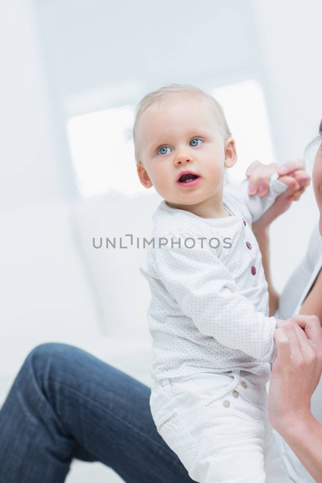 Mother holding a baby by his hands in living rrom
