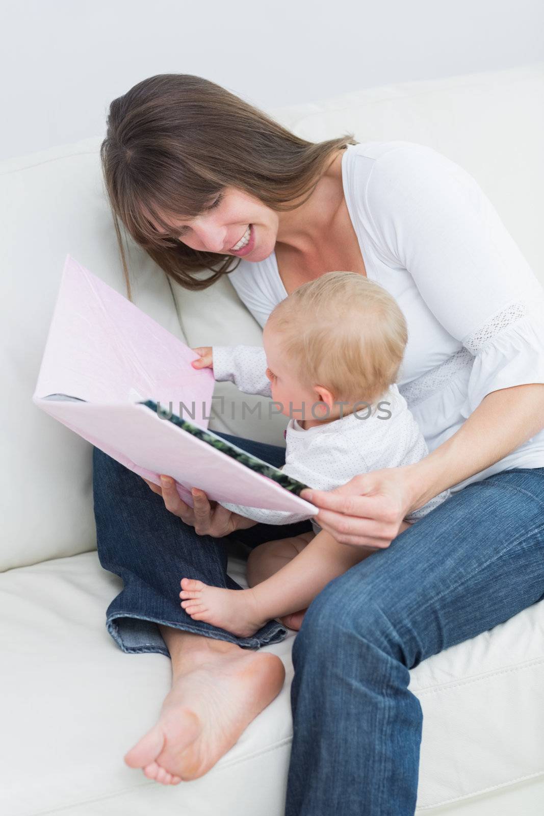 Baby holding a book with a mother in living room