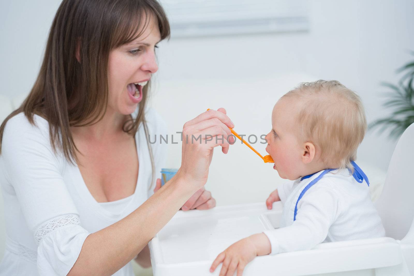 Mother feeding a baby while opening her mouth in living room