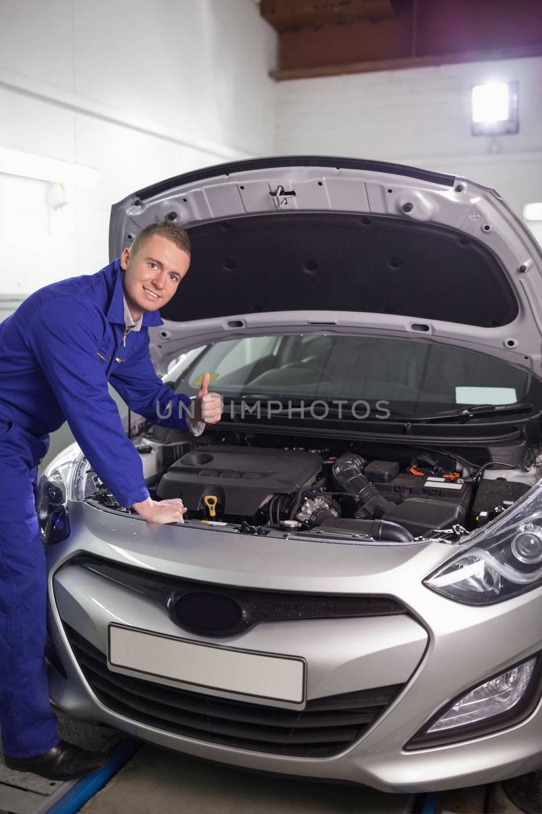 Mechanic leaning on a car with his thumb up in a garage