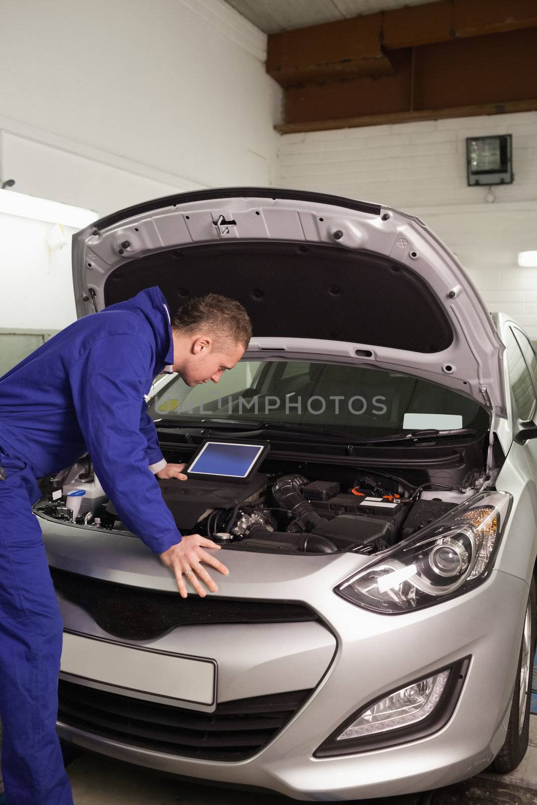 Concentrated mechanic looking at a car engine in a garage