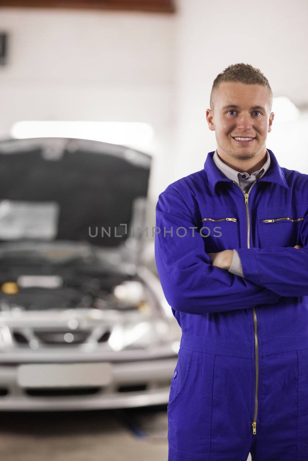 Smiling mechanicarms crossed next to a car by Wavebreakmedia