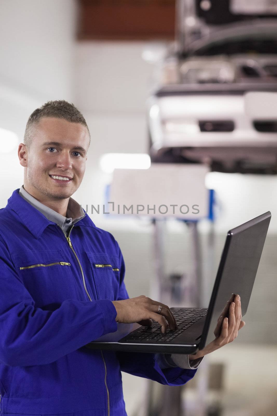 Smiling mechanic typing on a laptop in a garage