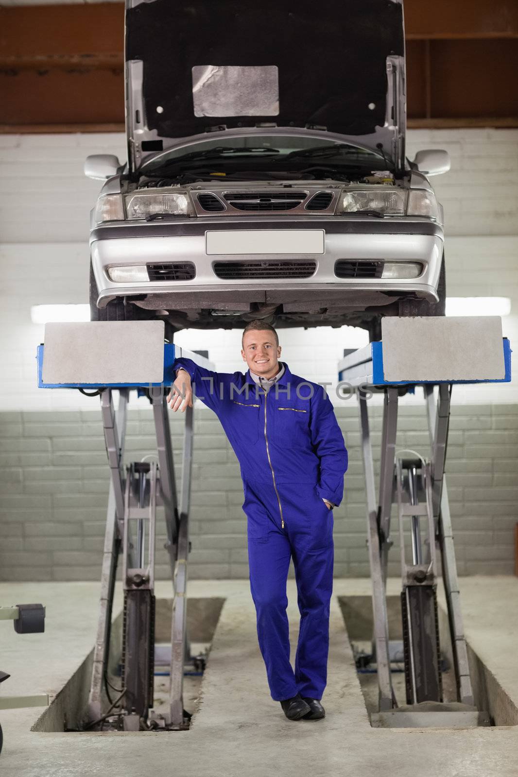 Smiling mechanic standing below a car in a garage