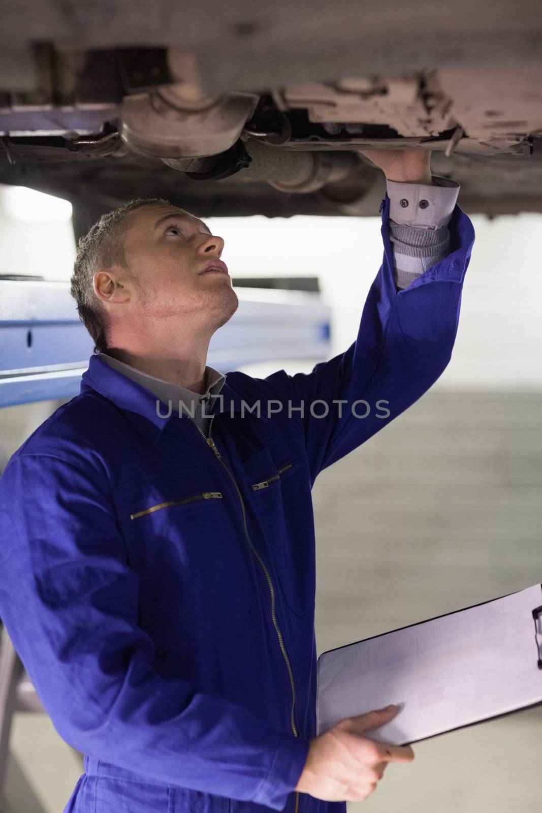 Mechanic touching the below of a car while holding a clipboard in a garage