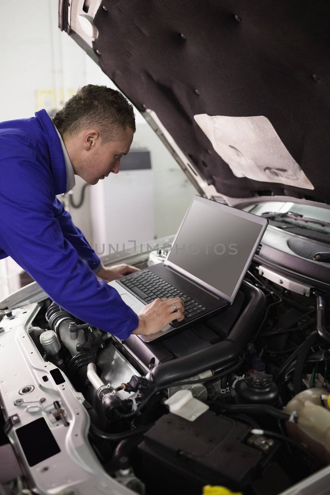 Mechanic looking at a computer on a car engine in a garage